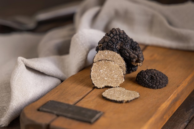 Whole and sliced black truffles mushroom on wooden board on dark brown table close up