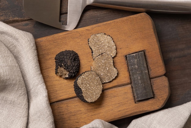 Whole and sliced black truffles mushroom on wooden board on dark brown table flat lay copy space