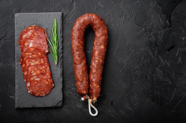 Whole and sliced chorizo sausage on black, flat lay with copy space