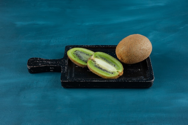 Whole and sliced kiwi fruits placed on a dark wooden board.