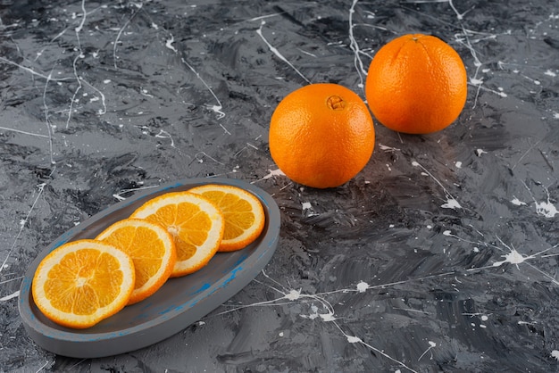 Whole and sliced orange fruits placed on a marble table .