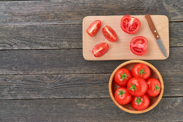 Whole and sliced organic red tomatoes on a cutting board, top view.