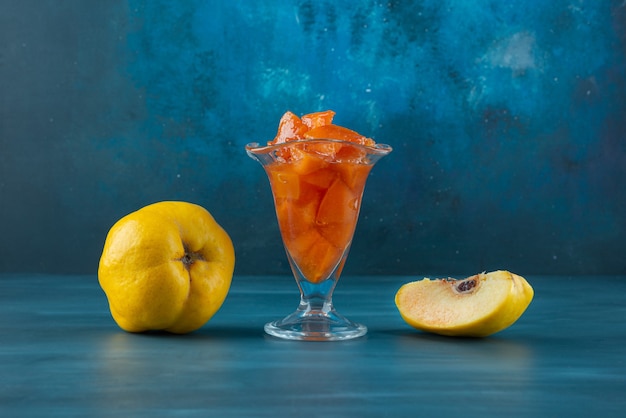 Whole and sliced quince fruits with a glass bowl of jam .