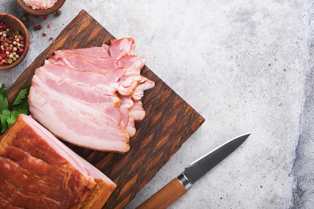 Whole Smoked Slab Bacon Brisket Sliced smoked gammon on a wooden table with rosemary parsley pepper salt and garlic on old gray concrete table background Copy space