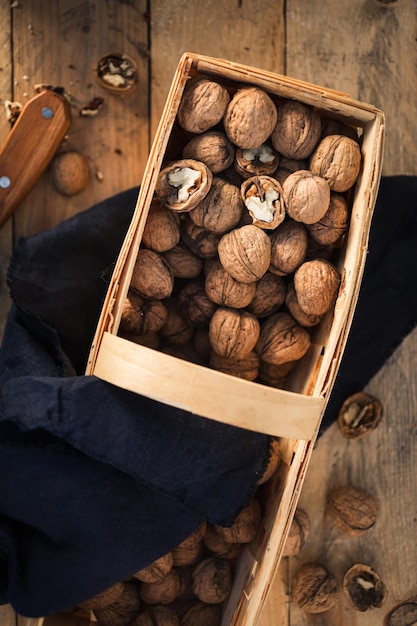 Whole walnuts and walnut pieces in wicker basket on wooden table