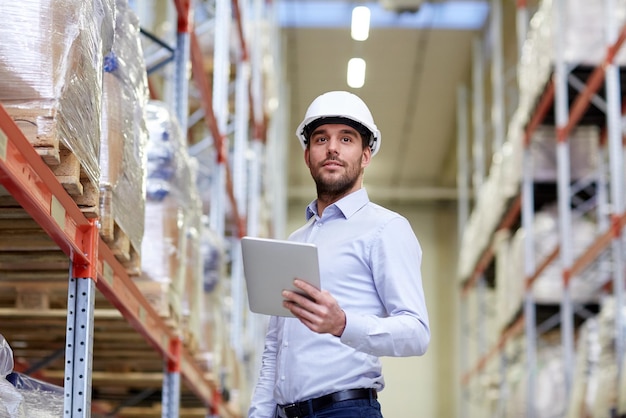 wholesale, logistic, business, export and people concept - happy man or manager with tablet pc computer checking goods at warehouse