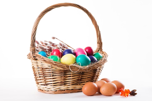 Wicker basket with colored eggs and willow branches on a white background Happy Easter