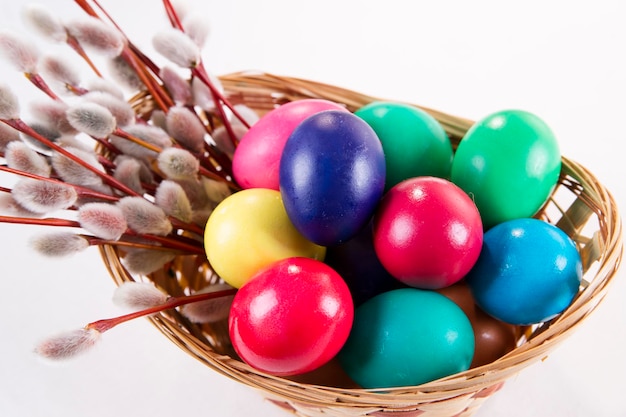 Wicker basket with colored eggs and willow branches on a white background Happy Easter