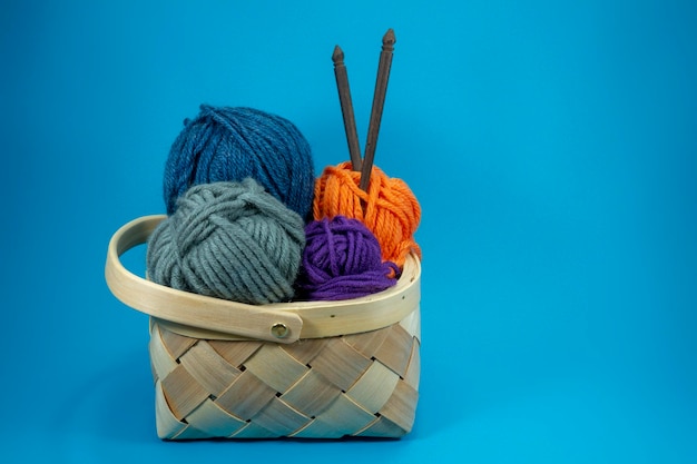 Wicker basket with colorful balls of yarn knitting needles on blue background with free copy space