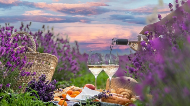 Wicker basket with delicious food for a romantic picnic in a lavender field The girl pours wine