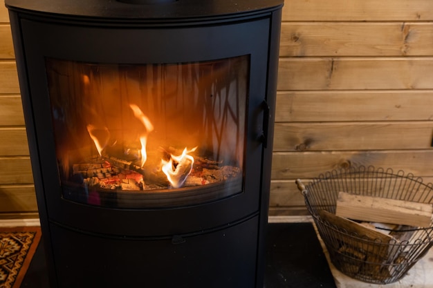 Wicker basket with firewood near fire chimney Wood stove fireplace with metal body and glass door in comfort house with cozy interior in room