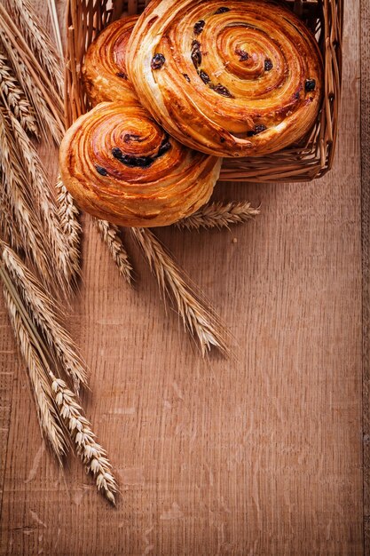 Wicker basket with raisin pastry wheat ears on oaken wooden board food and drink concept