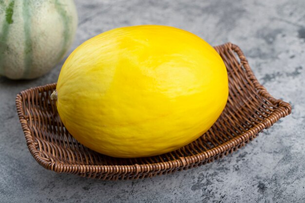 Wicker basket of yellow melon with cantaloupe melon on stone surface