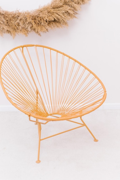 A wicker round chair stands against the wall Bright and spacious roomWicker chair handmade On the wall is a decoration made of dry reeds and grass