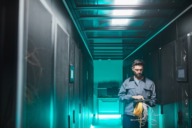 Wide angle portrait of mature network engineer using digital tablet in server room during maintenance work in data center, copy space