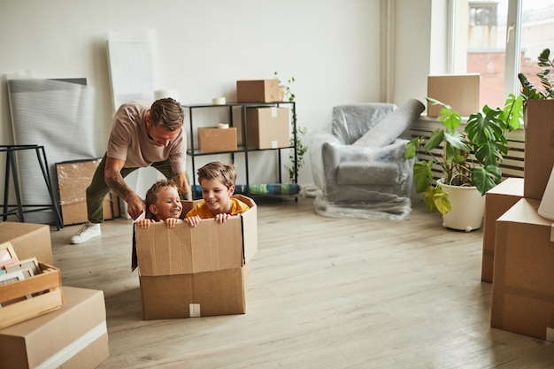 Wide angle portrait of two boys playing in big cardboard box while family moving to new house copy s...