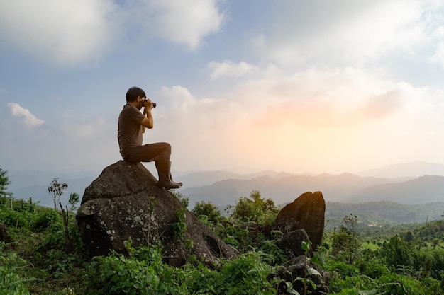 Wide angle shot of Asian man sitting on the rock and take photo relax adventure