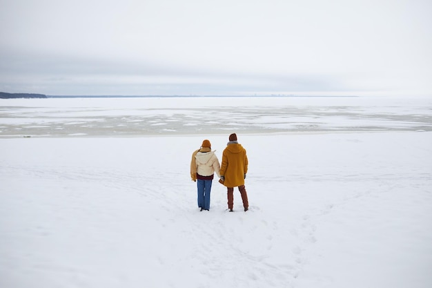 Wide angle shot of young couple standing by frozen sea and overlooking minimal winter landscape copy