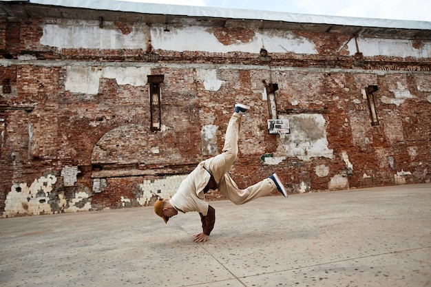 Wide angle shot of young man doing breakdance handstands outdoors in shabby urban setting copy space