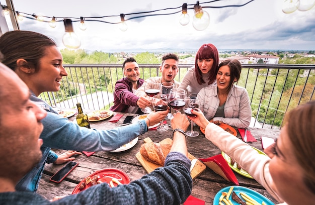 Wide angle view of happy people toasting red wine together at rooftop party in open air villa