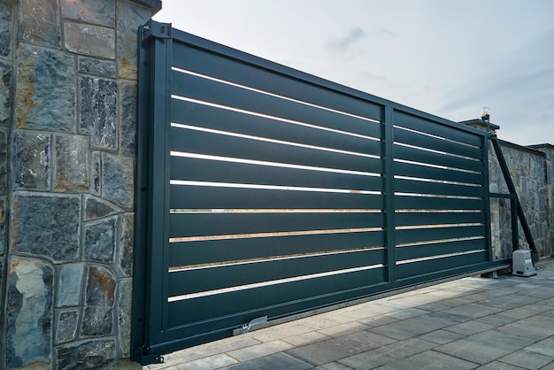 Wide automatic sliding gate with remote control installed in high stone fense wall Security and protection concept