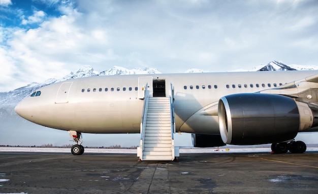 Wide body passenger airliner and boarding stairs at the airport apron on the background of mountains