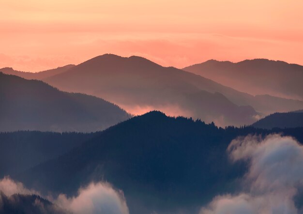 Photo wide panorama, fantastic view of covered with morning mist green carpathian mountains at sunset on bright clear orange sky . beauty of nature, tourism and traveling concept.