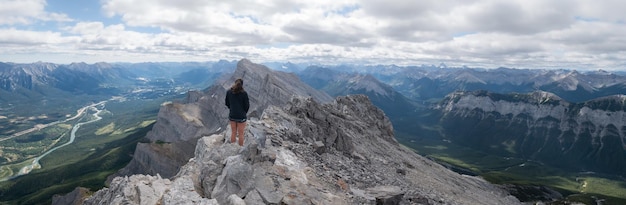 Wide panoramic shot of female hiker enjoying the views on valley from mountain summit