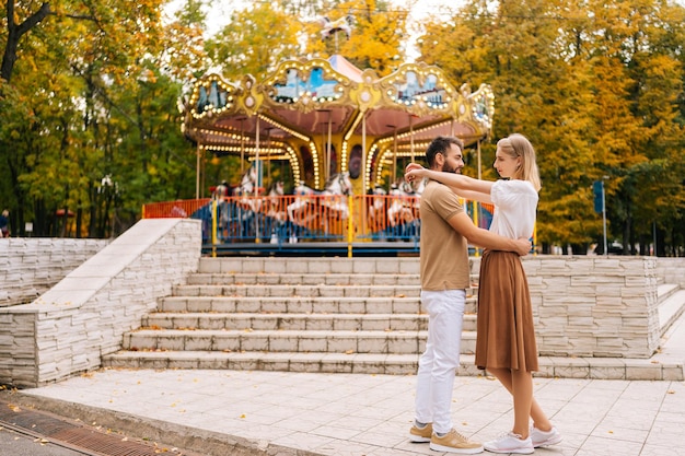 Wide shot of romantic young couple in love standing hugging looking at each other in amusement park in summer day