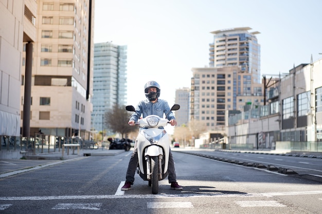 Wide shot of a young motorcyclist stopped at a traffic light in barcelona the man riding his scooter...