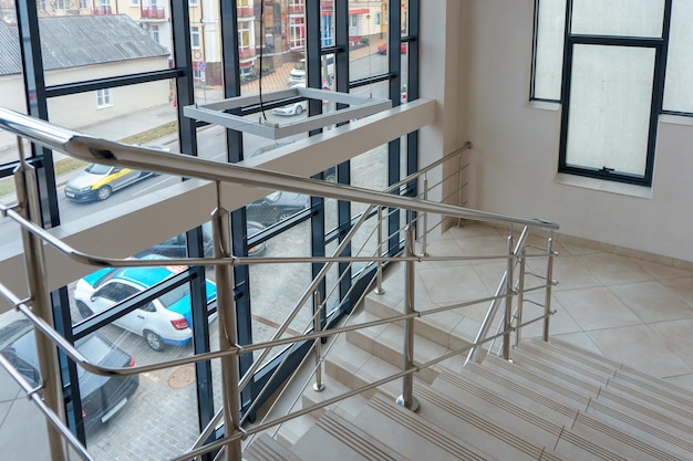 A wide staircase along the large windows in an office building Modern interior of the lobby of an office building with large spacious windows Illuminated long corridor in a modern business center