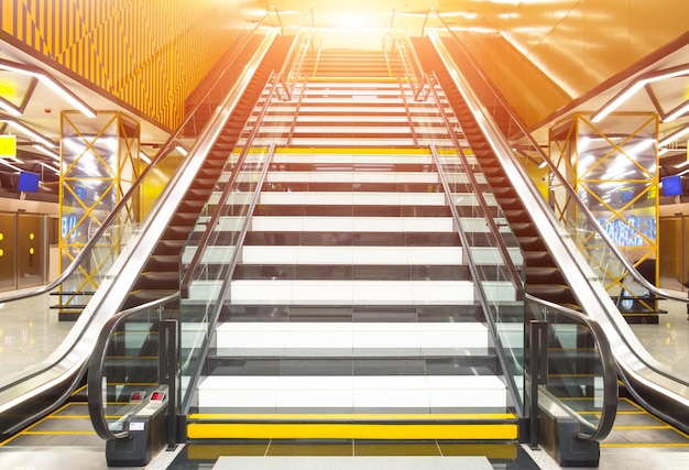 Wide staircase and on each side of it escalators leading up to the light