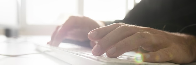 Wide view image of businessman programming using computer keyboard with bright windows in background and lens flare