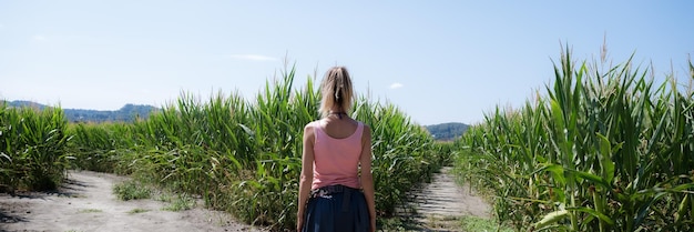 Wide view image of a young woman standinh in the middle of green corn fields