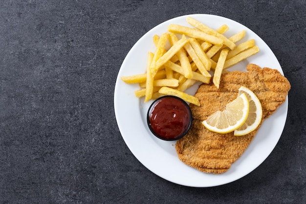 Wiener schnitzel with fried potatoes on black slate surface