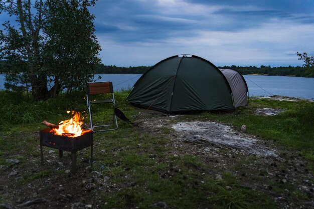 Wild camping in nature in Estonia A tent set on the shore of a rummu quarry a brazier with a fire Photo at dusk High quality photo