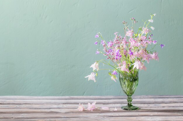 Wild flowers in green bocal on background green wall