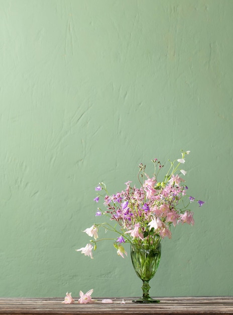 Wild flowers in green bocal on background green wall