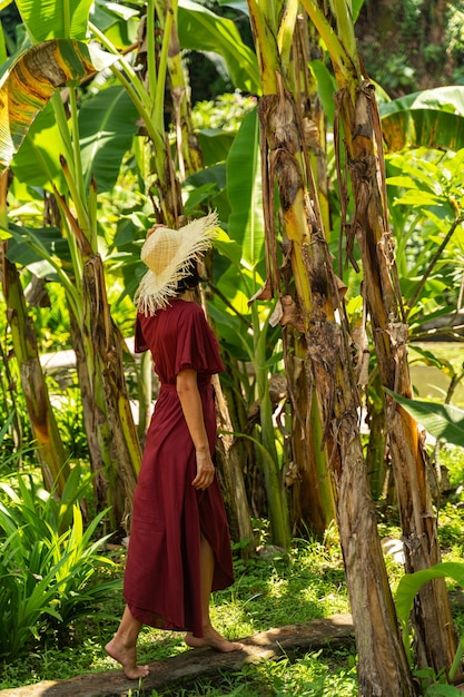 Wild nature. Amazing young female looking forward while enjoying bright green tropical plants, touching her hat