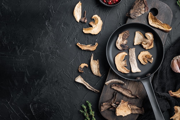 Photo wild organic dried porcini mushroom set in cast iron frying pan, on black