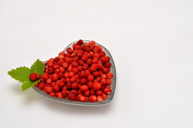 Wild strawberries in a heartshaped bowl on a white background and place for text