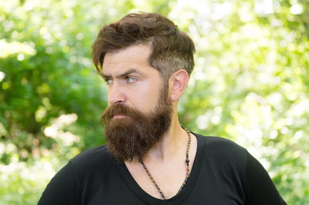 Wilderness survival guide. Man bearded hipster bright foliage background. Guy relax in summer forest. Handsome man with beard and mustache summer vacation. Summer heat season concept. Facial care.