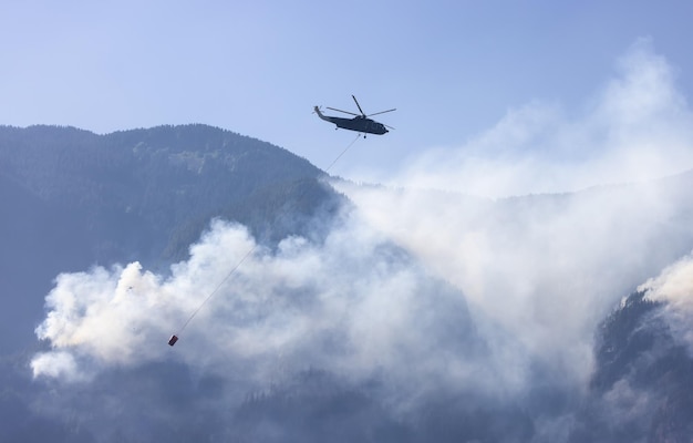 Wildfire Service Helicopter flying over BC Forest Fire and Smoke on the mountain near Hope