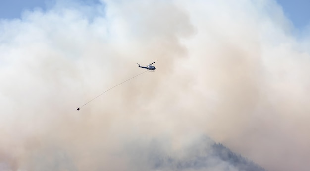 Wildfire Service Helicopter flying over BC Forest Fire and Smoke on the mountain near Hope