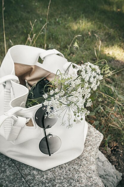 Photo wildflowers sunglasses and a smartphone are in a white womens bag on the grass