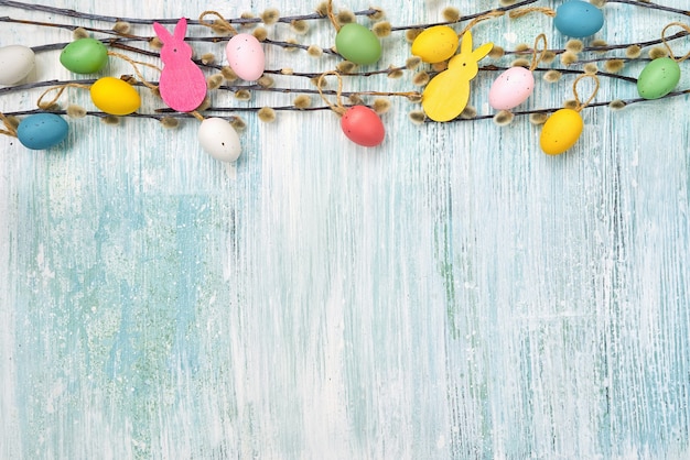 Willow branch and decorative Easter eggs on blue wall. Top view, copy space