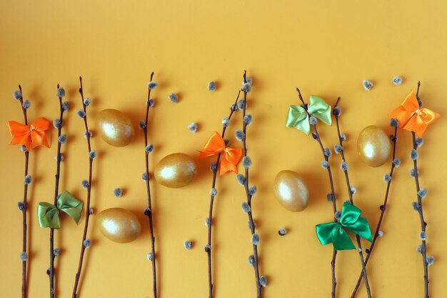 Willow branches colorful bows made of satin ribbons golden eggs on a yellow background top view space for text