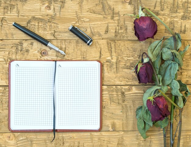 Wilted roses with a notebook and fountain pen on a rustic table.