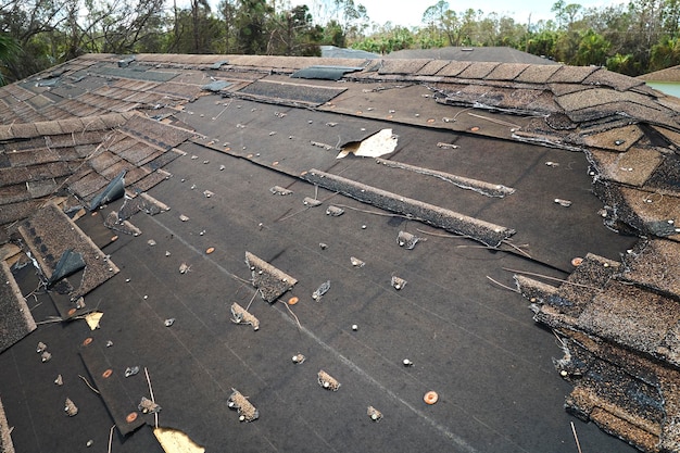 Wind damaged house roof with missing asphalt shingles after hurricane Ian in Florida Repair of home rooftop concept