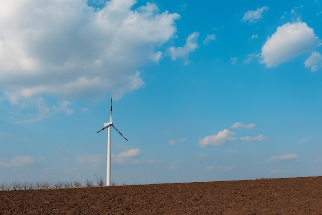 Wind turbine in agricultural field windmill generating green energy Background of blue sky Fertile soil land